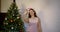 Adult woman with headband with pink rabbit ears is taking selfies by cell phone near Christmas tree