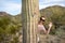 Adult woman hides and waves while standing behind a large saguaro cactus in the Sonoran Desert