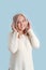 An adult woman listens to music in wireless headphones standing on a blue background. Vertical photo