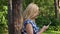 Adult woman looking in mobile phone while walking in green park at summer day