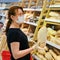 Adult woman in medical mask buys a loaf of bread in a supermarket