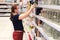 Adult woman in a medical mask chooses household goods in a store. Buying cans in a supermarket