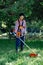 Adult woman mows the grass in the backyard using string trimmer. Garden work concept