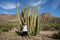 Adult woman picking her nose next to a large organ pipe cactus in Arizona