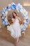 Adult woman plays the block flute while sitting on a swing in flowers. Studio portrait of musician woman in white dress