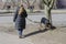 An adult woman walks with her pet on a leash along a city street