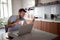 Adult young man with beard wearing glasses,  watching his cell phone, smiling  in front of laptop on table.  lifestyle, modern,