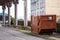 Advanced electrical powered rubbish trash skip bin in a street. Brown color. Control panel in the back. Construction and