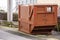 Advanced electrical powered rubbish trash skip bin in a street. Brown color. Control panel in the back. Construction and