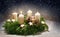 Advent wreath from evergreen branches with white candles, the first is burning for the time before Christmas, dark snowy