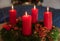 Advent wreath made of green yew twigs, with four lighted red candles and ribbon at home