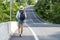 Adventure recreation and travel transport concept. Young woman wearing hat carrying backpack while walking alone on the roadside