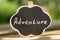 Adventure waiting for you concept - small sign with Adventure inscription outdoors, green blurred background