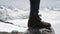 Adventurer feet in leather boot stomps on stone at snowy mountain scenic view