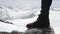 Adventurer feet in leather boot stomps on stone at snowy mountain scenic view