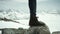 Adventurer feet in leather shoe stomps on rock at snowy mountain scenic view