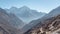 Adventurer with a red backpack on a rocky mountain path with snow capped peaks in the distance