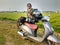 Adventurous biker with loaded scooter and backpack poses amidst Uttarakhand\\\'s scenic farmlands. Explore the rural charm