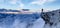 Adventurous Man Hiker standing on top of icy peak with rocky mountains in background.