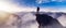 Adventurous Man Hiker standing on top of peak with rocky mountain in background.