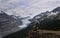 Adventurous man hiker on the steep cliff over Columbia Icefield glacier and a moraine lake.