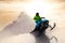 Adventurous Man Riding a Snowmobile in white snow during a colorful sunset