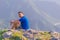 Adventurous man sitting on top of a mountain and enjoying the beautiful view, while looking downhill at the blue river and amazing