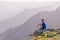 Adventurous man sitting on top of a mountain and enjoying the beautiful view, while looking downhill at the blue river and amazing
