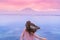 Adventurous young woman blown by the wind looks at the ocean and mountains in the distance. Agung volcano at sunset