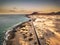 Aerial above view of yellow tropical sandy beach with black long way road and car traveling - ocean blue waves and shore - sunset