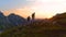 AERIAL: Active young tourists hiking up a grassy mountain in the Alps at sunset.