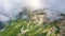 Aerial approaching view of stunning Caucasian mountains covered with grass, snow and stones under steam of huge clouds