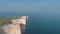 An aerial backward view of the Old Harry Rocks along beautiful huge white cliffs and crystal blue water under an amazing hazing bl