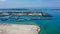 Aerial of beach, pier, boats, resort and businesses on tip of Tanyung Benoa Peninsula above dark blue water. Green