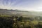 Aerial birds-eye across the misty afternoon sun landscape with distant mountains and suburbia