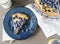 Aerial of blueberry tart on blue plate, on tabletop with napkin.