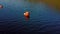 Aerial camera floats past two orange buoys low over pristine blue waters