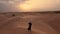 AERIAL. Camera following woman in traditional Emirati dress walking in a desert in strog wind and sunset.