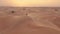 AERIAL. Camera following woman in traditional Emirati dress walking in a desert in strog wind and sunset.