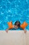 Aerial child with armbands holding on to the curb of the pool