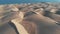 AERIAL. Cinematic flight over the desert at sunset - the tops of the sand dunes cast shadows. Panorama of the natural