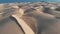 AERIAL. Cinematic flight over the desert at sunset - the tops of the sand dunes cast shadows. Panorama of the natural