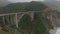 Aerial cinematic footage of high bridge on coastal panoramic road. Cars passing through Bixby Creek Bridge. California