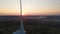 Aerial close up view of rotating blades of wind turbine against scenic sunset, the sun goes down over horizon