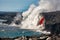 Aerial daytime view of top portion of waterfall shaped flow of red lava from volcano in Hawaii and the rocky beach below