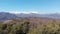 Aerial: drone ascending from forest reveals aerial view of snow capped mountains valley and clear blue sky