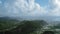 Aerial drone flies over wooded mountains with a settlement and a winding road, near the sea and foggy horizon (Saint