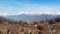 Aerial: drone flying over forest in springtime, aerial view of snow capped mountain range and valley on the Alps, clear blue sky,