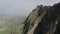 Aerial drone footage of majestic rock with green vegetation against misty valley at background. Splendid wild nature in