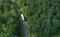 Aerial drone perspective view on white truck with cargo trailer riding through the forest on curved asphalt road